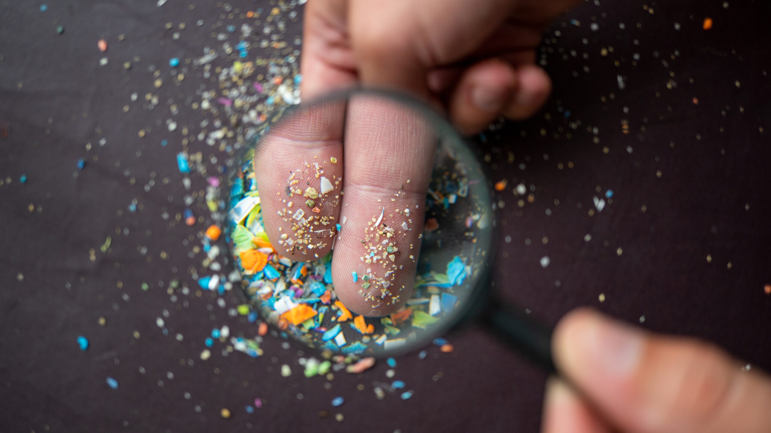 Close-up of micro plastic particles on the fingers under a magnifying glass.