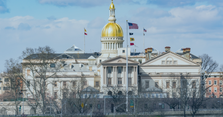 New Jersey state capital building with a gold dome viewed behind leafless trees.